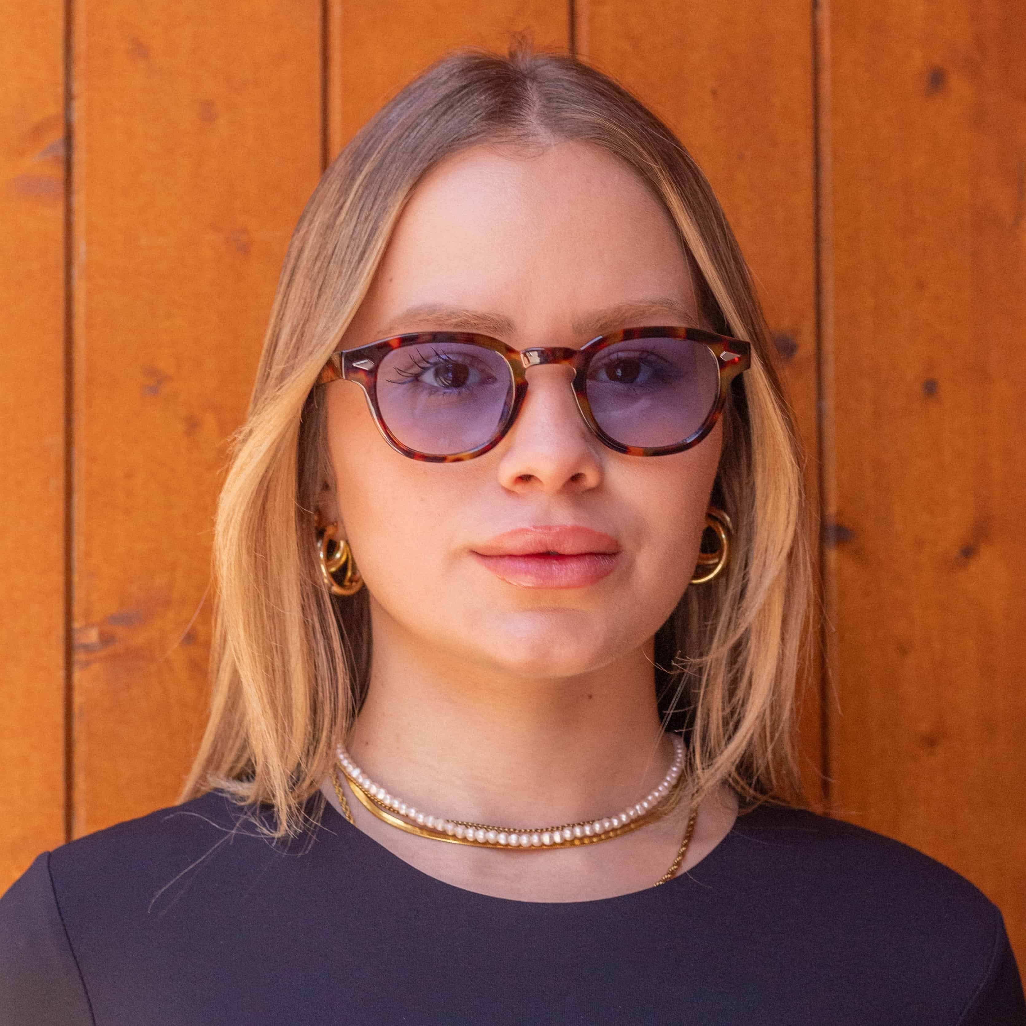 Aqua Tortoise sunglasses with gradient blue lenses worn by a woman against a wooden backdrop.