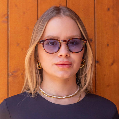 Aqua Tortoise sunglasses with gradient blue lenses worn by a woman against a wooden backdrop.