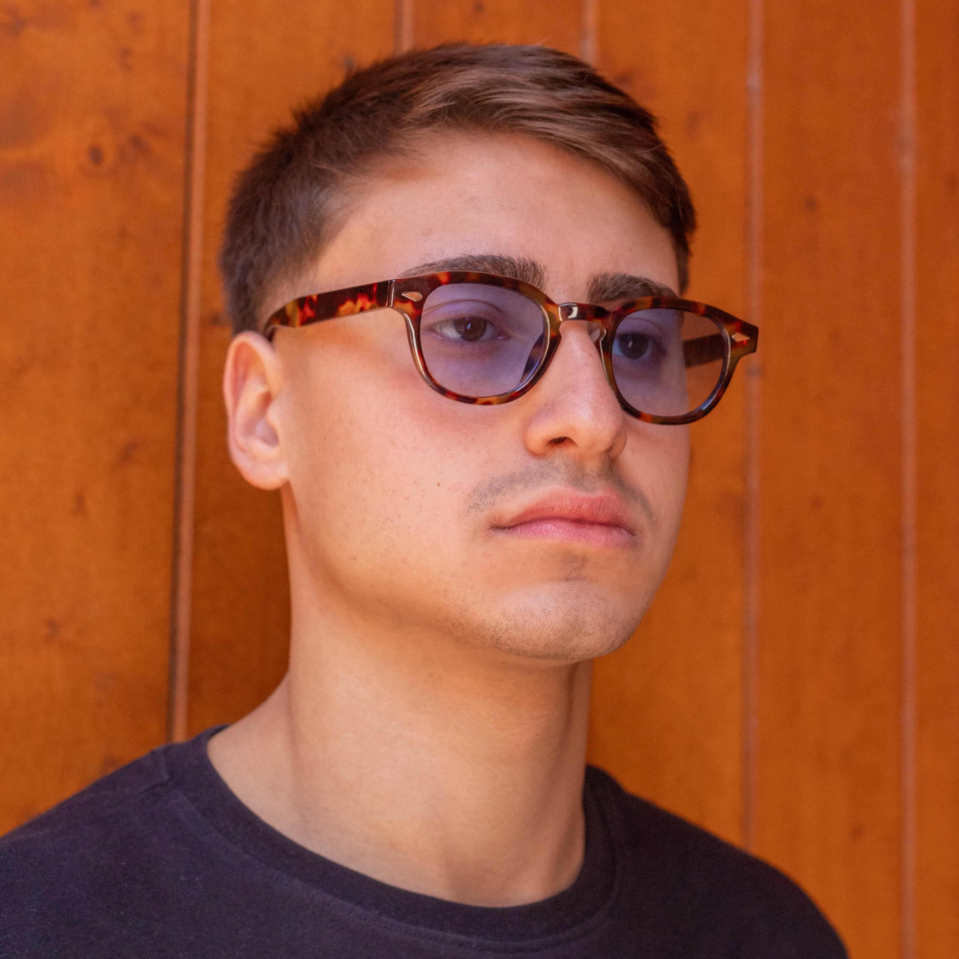 Young man wearing Aqua Tortoise sunglasses with gradient blue lenses against a wooden background.