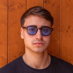 Man wearing stylish Deep Tortoise sunglasses with gradient blue lenses against a wooden background.